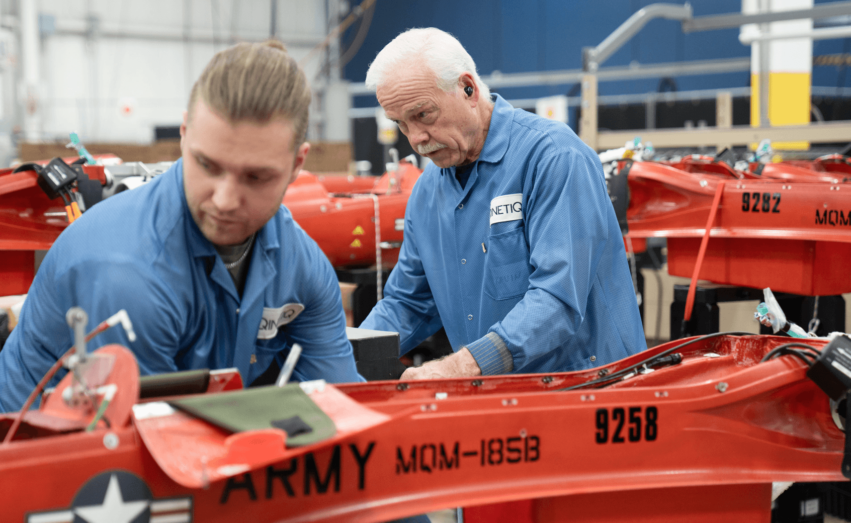 Two men in blue work shirts assemble red MQM-185B target drones
