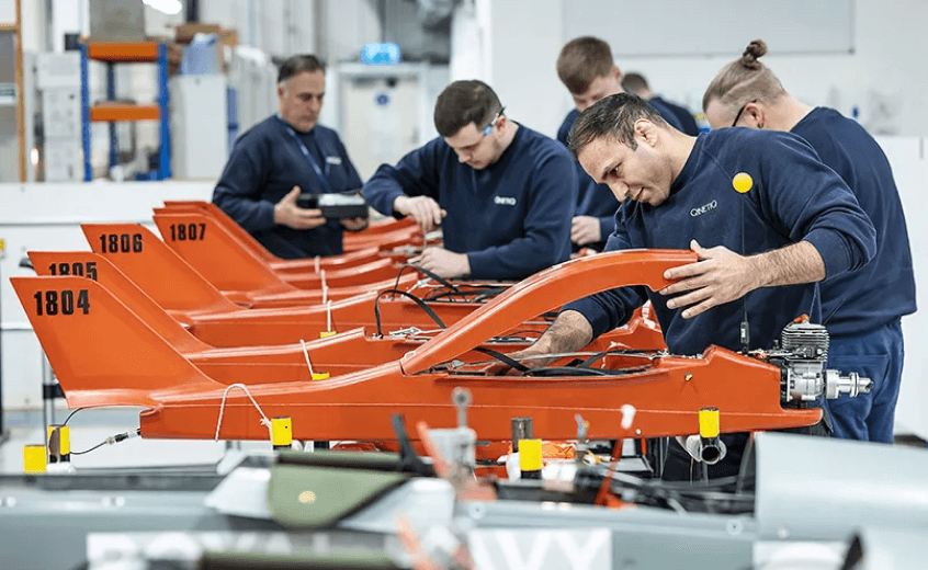 Engineers assembling a row of orange unmanned aerial vehicles in a workshop